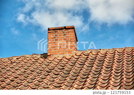 Red brick chimney designed on the roof of residential house or building outside against a cloudy sky background with copyspace. Air vent construction for the release of smoke and heat from fireplace 121759153