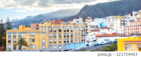 Scenic landscape view of vibrant houses, traditional residential buildings or city structures. Tourism destination street on Santa Cruz road, La Palma, Spain with background mountains and cloudy sky 121759403