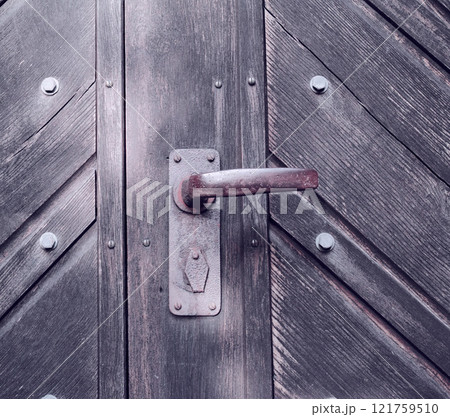 A strange old wooden entrance door with a rusted door handle. A vintage door knob. Closeup of a traditional door with a handle and a lock. A copy space background. The gate knob is made of metal. A strange old wooden entrance door with a rusted door handle. A vintage door knob. Closeup of a traditional door with a handle and a lock. A copy space background. The gate knob is made of metal. 121759510