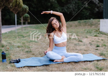 Young woman practicing yoga stretching in park on a mat 121762182