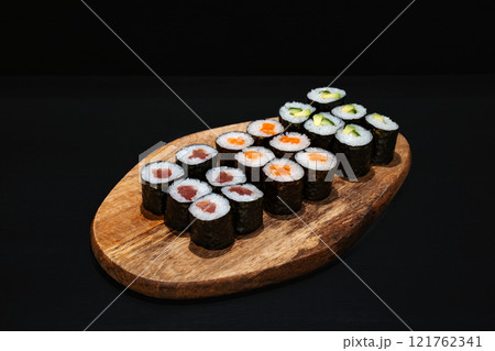 Creative minimalist display of assorted Maki sushi rolls on a wooden platter against a dark backdrop, emphasizing vibrant colors and exquisite Japanese culinary art with a modern aesthetic. Creative minimalist display of assorted Maki sushi rolls on a wooden platter against a dark backdrop, emphasizing vibrant colors and exquisite Japanese culinary art with a modern aesthetic. 121762341
