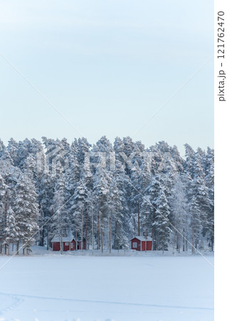 Snowy forest, two red cabin houses in the forest, winter landscape in Finland Snowy forest, two red cabin houses in the forest, winter landscape in Finland 121762470
