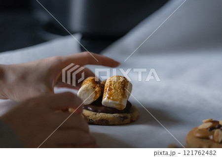 Woman hand taking homemade american chocolate chip cookie with burnt marshmallows from white baking paper. Woman hand taking homemade american chocolate chip cookie with burnt marshmallows from white baking paper. 121762482