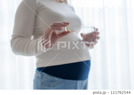Pregnant woman holding a glass of water and taking vitamins during pregnancy. Pregnancy, health, pharmaceuticals, care. Close up Pregnant woman holding a glass of water and taking vitamins during pregnancy. Pregnancy, health, pharmaceuticals, care. Close up 121762544