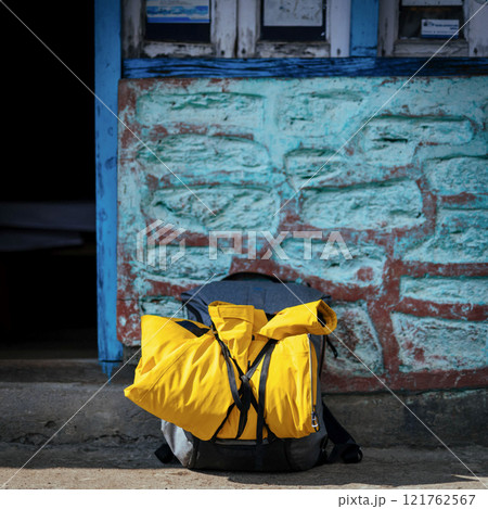 A yellow backpack rests quietly near a blue weathered wall. Concept of travel, exploration, and the essence of adventure. 121762567