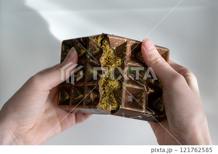 Dubai chocolate with pistachio, tahini and kadaif, chocolate broken in woman's hands 121762585