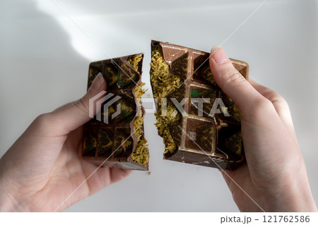 Trend Dubai chocolate with pistachio, tahini and kataifi dough, chocolate broken in woman's hands. Handmade confectionary 121762586