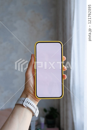 Close-up of human hand holding black white-screen mobile phone in interior background. mockup 121762895