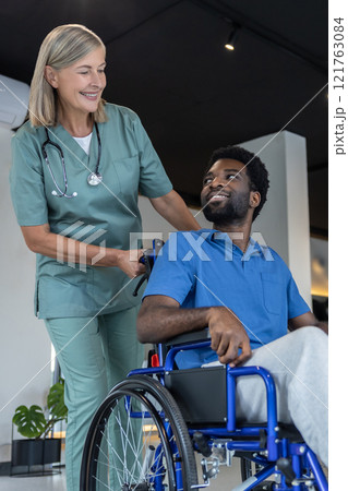Mature female doctor carrying a wheeling-chair with a male patient 121763084