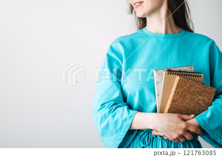 Smiling woman holding eco-friendly notebooks in minimalist style. Sustainable stationery trends, cork accessories, and conscious consumerism for a zero-waste lifestyle. 121763085