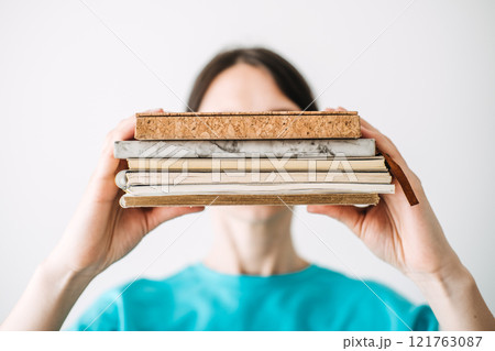 Young woman holding a stack of notebooks with unique textures and materials in a bright minimalist background. Creative journaling and mindful self-expression. Young woman holding a stack of notebooks with unique textures and materials in a bright minimalist background. Creative journaling and mindful self-expression. 121763087