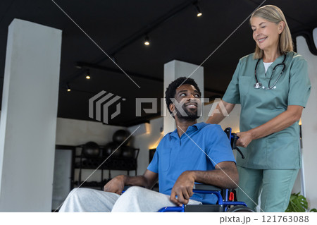 Mature female doctor carrying a wheeling-chair with a male patient Mature female doctor carrying a wheeling-chair with a male patient 121763088