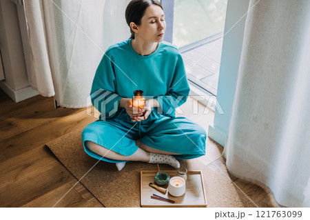 Woman holding candle during a moment of stillness in serene home setting. The ritual of stillness, modern spirituality, and energy cleansing. Woman holding candle during a moment of stillness in serene home setting. The ritual of stillness, modern spirituality, and energy cleansing. 121763099