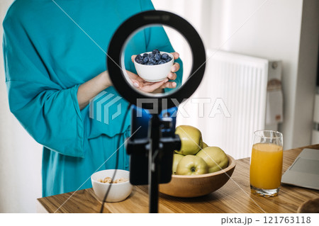 Woman presenting fresh blueberries with a ring light setup. Content creation at home, vlogging essentials, and personal branding tools. 121763118