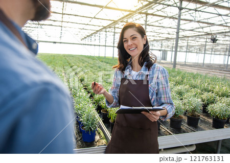 Smiling young woman in apron talking to a man and looking positive 121763131