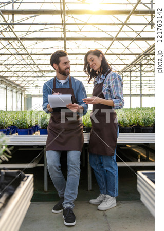 Man and woman working in greenhouse and discussing something Man and woman working in greenhouse and discussing something 121763142