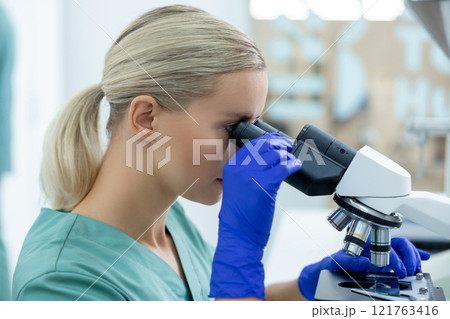 Medical woman wearing gloves working in sterile laboratory using microscope and optical tools 121763416