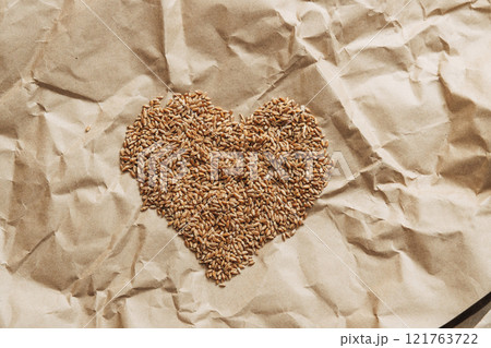 Golden wheat grains in the shape of a heart lie on a background of craft paper 121763722