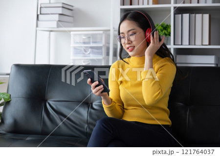 Young Woman Relaxing Happily in the Living Room with Headphones and Smartphone, Enjoying Music and Leisure Time Young Woman Relaxing Happily in the Living Room with Headphones and Smartphone, Enjoying Music and Leisure Time 121764037