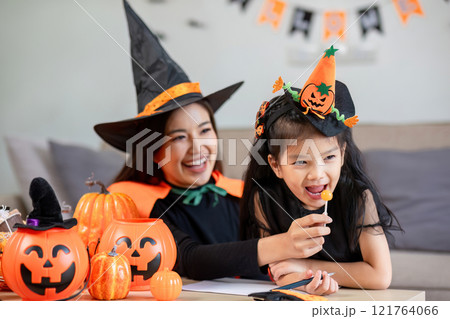 Mother and Child Enjoying Halloween Activities Together in Matching Witch Costumes with Pumpkins and Decorations 121764066