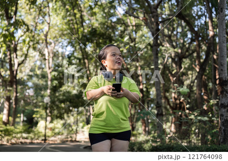 Energetic Woman Jogging Through a Lush Garden Path Surrounded by Vibrant Greenery and Sunlight 121764098