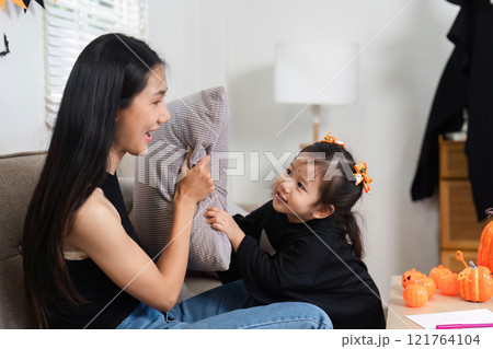 Adorable Mother and Daughter Dress Up and Decorate Living Room for Halloween with Joyful Smiles and Festive Decorations 121764104