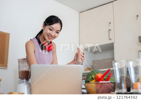 Young Woman Embracing a Healthy Lifestyle by Preparing a Fresh Fruit Smoothie in a Modern Kitchen Setting 121764502