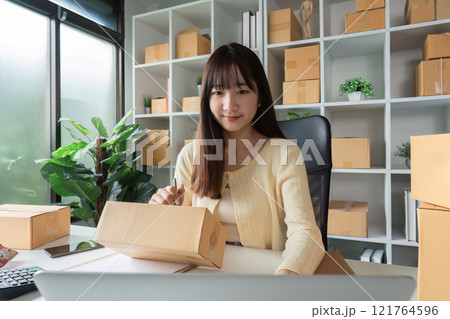 Young Woman Taking Online Sales Order in a Modern Home Office Surrounded by Shipping Boxes and Green Plants 121764596