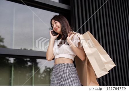 Young Woman Enjoys Shopping Day with Eco-Friendly Paper Bag in Urban Setting Young Woman Enjoys Shopping Day with Eco-Friendly Paper Bag in Urban Setting 121764779