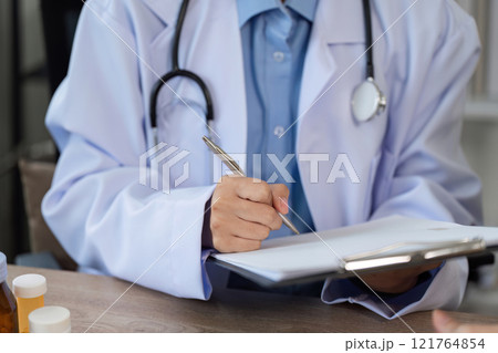 Doctor in White Coat Recording Patient's Symptoms with Pen and Clipboard in Medical Office Setting 121764854