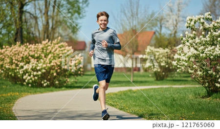 Caucasian teen boy running in spring park for fitness and wellbeing 121765060