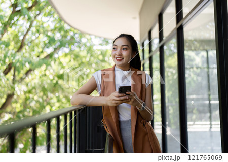 Woman smiling while using smartphone on balcony urban environment lifestyle bright daylight viewpoint 121765069