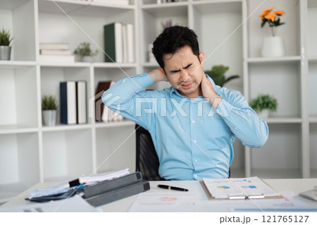 Office Worker Experiencing Office Syndrome with Muscle Aches and Pains at Desk in Modern Workplace Environment 121765127