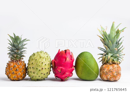 Exotic fresh summer fruits on white background. Dragon fruit, pineapple, persimmon, mango, annona cherimola flat lay with free copy space. Exotic fresh summer fruits on white background. Dragon fruit, pineapple, persimmon, mango, annona cherimola flat lay with free copy space. 121765645
