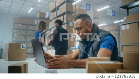 African American post office employee scans parcels with barcode scanner, enters data on laptop African American post office employee scans parcels with barcode scanner, enters data on laptop 121765918