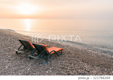 Plastic sun beds with orange capes on the sea beach at sunrise. Summer vacation concept. Plastic sun beds with orange capes on the sea beach at sunrise. Summer vacation concept. 121766269