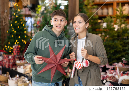 Girl with guy buyer considers New Year and Christmas decorations ornaments for Christmas tree Girl with guy buyer considers New Year and Christmas decorations ornaments for Christmas tree 121768183