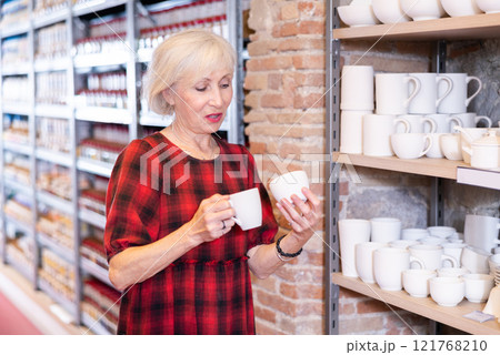 Elderly woman chooses pottery clay cup 121768210