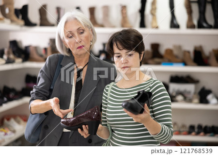 Two women are shopping in shoe store, choose woman dress shoes, classic shoes Two women are shopping in shoe store, choose woman dress shoes, classic shoes 121768539