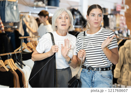Girl and senior woman buyer noticed desired product in clothes store and smiles from purchase Girl and senior woman buyer noticed desired product in clothes store and smiles from purchase 121768607