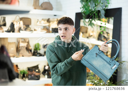 Guy customer is amazed to read price tag on leather handbag in store 121768636