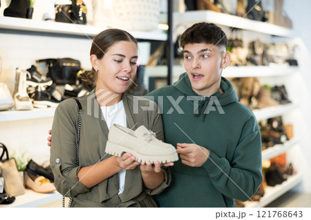 Cheerful young couple choosing comfortable womens loafers in shoe store 121768643