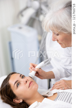 Young woman having face laser therapy procedure by specialist 121768718