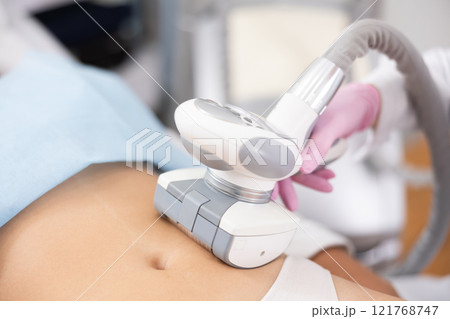 Faceless female doctor doing Rf lifting procedure on belly of young woman in beauty salon. Treatment of flabby skin Faceless female doctor doing Rf lifting procedure on belly of young woman in beauty salon. Treatment of flabby skin 121768747