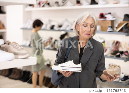Elderly woman chooses sneakers in shoe store Elderly woman chooses sneakers in shoe store 121768748