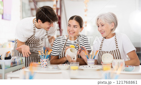 Group of cheerful people painting ceramic dishware in pottery class 121768861