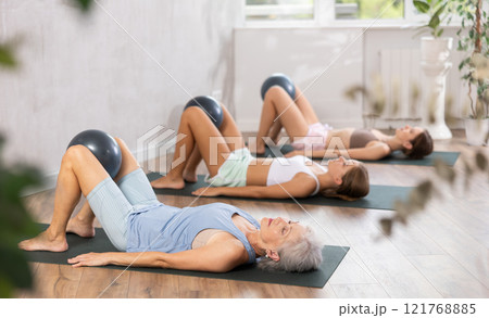 Fitness family in activewear working out with soft ball pilates on mat while doing upper body training in yoga studio Fitness family in activewear working out with soft ball pilates on mat while doing upper body training in yoga studio 121768885