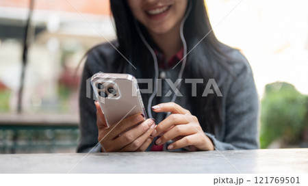 A woman enjoys listening to music on her earphones and using her smartphone while sitting outdoor. 121769501