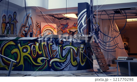 Empty abandoned warehouse with graffiti paintings on walls, concept of alternative lifestyle. City slums ghetto location used as crime haven by anti establishment protestors doing street art 121770298