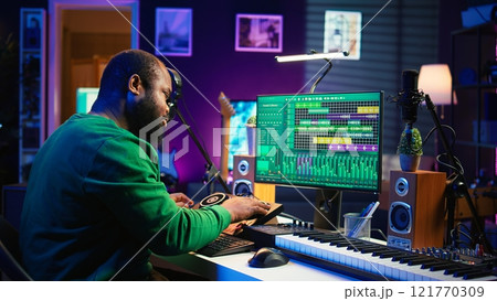 Skilled male composer producing new songs on his mixing console, operating on professional gear in home studio. Artist audio engineer twisting knobs to adjust sound levels on tracks. Camera B. Skilled male composer producing new songs on his mixing console, operating on professional gear in home studio. Artist audio engineer twisting knobs to adjust sound levels on tracks. Camera B. 121770309